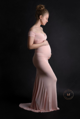 maternity photo of woman in light pink dress with black background in lapeer photography studio